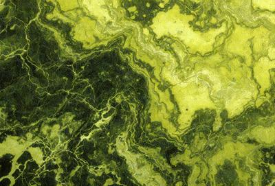 The primary subject of the image is a close-up of a green and yellow marble surface. The setting is a rocky environment, with the marble surface being the main focus. The visual style is a close-up of the marble, showcasing its intricate patterns and textures. The colors and mood of the image are predominantly green and yellow, giving it a natural and earthy feel.