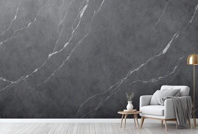 The primary subject of the image is a large gray marble wall. The setting is a living room with a couch and a chair. The visual style is a photo of the living room with the gray marble wall as the main focus. The colors and mood of the image are predominantly gray, creating a calm and sophisticated atmosphere.