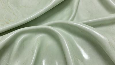 The primary subject of the image is a green fabric, which appears to be a piece of marble or a similar material. The setting is a room with a table, and the visual style is a close-up of the fabric. The colors and mood of the image are predominantly green, giving it a calm and serene atmosphere.