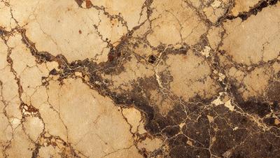 The primary subject of the image is a close-up of a marble surface with a pattern of brown and yellow colors. The setting is a stone wall, and the visual style appears to be a photo. The colors and mood of the image are warm and earthy, with a sense of texture and depth.