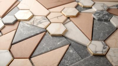 The primary subject of the image is a marble tile floor with a geometric pattern. The setting is a room with a marble wall, and the visual style is a close-up of the floor. The colors and mood of the image are predominantly neutral, with the marble tiles providing a sense of elegance and sophistication.