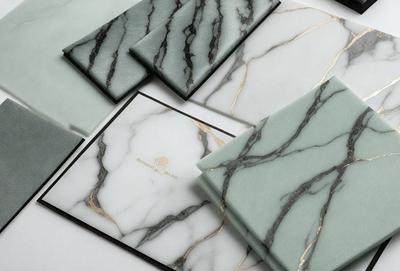 The primary subject of the image is a collection of marble-patterned books and cards. The setting is a white table, and the visual style is a combination of photo and digital art. The colors and mood of the image are predominantly white and gray, with a touch of gold, giving it a sophisticated and elegant appearance.