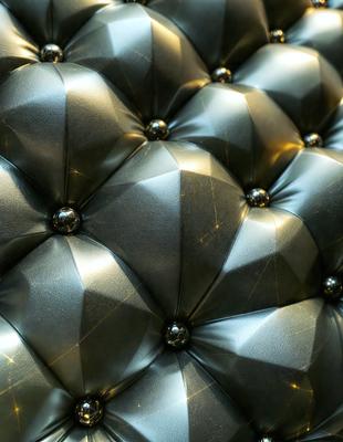 The primary subject of the image is a large, shiny, and metallic cushion. The setting is a room with a couch, and the visual style is a close-up of the cushion. The colors and mood of the image are predominantly silver and shiny, giving it a modern and sleek appearance.