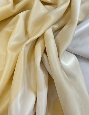 The primary subject of the image is a large piece of white fabric, possibly a sheet or a curtain. The fabric is folded and draped over a surface, creating a visually interesting and textured appearance. The setting appears to be a room or a space where the fabric is displayed, possibly for decoration or storage. The visual style of the image is a close-up of the fabric, showcasing its details and texture. The colors and mood of the image are predominantly white, giving it a clean and