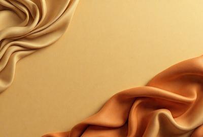 The primary subject of the image is a piece of fabric, possibly a piece of silk, with a yellowish hue. The setting is a wall, and the visual style appears to be a close-up of the fabric. The colors and mood of the image are warm and inviting, with the yellowish hue creating a sense of warmth and comfort.