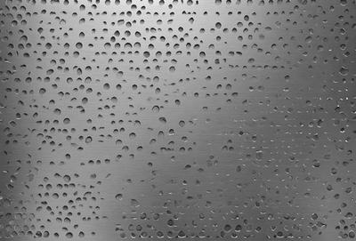 The primary subject of the image is a close-up of a metal surface with a pattern of holes. The setting is a dark room, and the visual style appears to be a photo. The dominant colors are silver and black, creating a moody atmosphere.