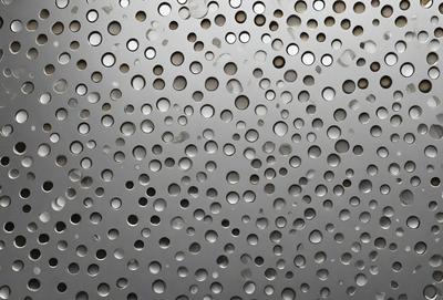The primary subject of the image is a close-up of a metal surface with numerous small holes. The setting is a metal surface, and the visual style is a close-up of the metal. The dominant colors are silver and black, and the overall atmosphere is a combination of industrial and textured.