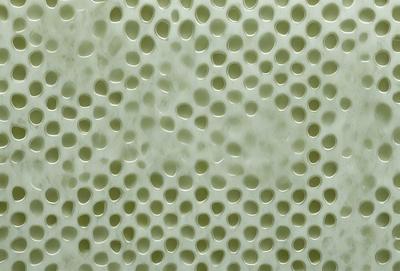 The primary subject of the image is a close-up of a white, textured surface with numerous small holes. The setting appears to be a wall or a similar surface, and the visual style is a close-up of the textured surface. The dominant colors are white and green, creating a clean and fresh atmosphere.