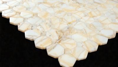 The primary subject of the image is a white marble tabletop with a unique hexagonal pattern. The tabletop is set against a dark background, which highlights the intricate design of the marble. The visual style of the image is a close-up of the marble tabletop, showcasing the details of the hexagonal pattern. The colors and mood of the image are predominantly dark, with the white marble serving as a striking contrast against the black background.