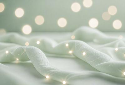 The primary subject of the image is a white sheet with a pattern of white dots. The sheet is laying on a bed, which is the setting and background of the scene. The visual style of the image is a photo, and the dominant colors are white and green, creating a calm and soothing atmosphere.