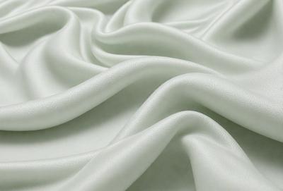 The primary subject of the image is a white sheet of fabric, which is the main object, scene, or focus of the image. The setting or background is a white surface, which provides a clean and minimalistic backdrop for the fabric. The visual style of the image is a close-up of the fabric, showcasing its texture and details. The colors and mood of the image are predominantly white, giving it a clean, fresh, and serene atmosphere.