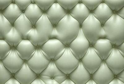 The primary subject of the image is a large, white, and green cushion. The cushion is made of a soft, plush material and features a pattern of white and green circles. The setting is a room with a green wall, and the visual style is a close-up of the cushion. The colors and mood of the image are predominantly green, creating a calm and soothing atmosphere.