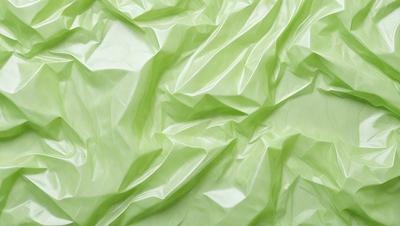 The primary subject of the image is a close-up of a green plastic sheet. The sheet is wrinkled and has a slightly textured appearance. The setting is a table, and the visual style is a close-up of the plastic sheet. The colors are predominantly green, and the overall atmosphere is somewhat industrial or utilitarian.