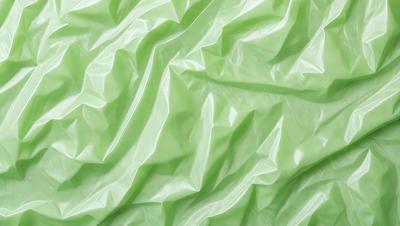 The primary subject of the image is a green sheet of plastic, which is the main object, scene, or focus of the image. The setting/background consists of a green surface, possibly a table or a wall, where the plastic is placed. The visual style of the image is a close-up of the green plastic, showcasing its texture and color. The colors and mood of the image are predominantly green, giving it a fresh and natural atmosphere.