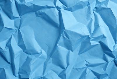 The primary subject of the image is a blue piece of paper with a wrinkled texture. The setting is a blue background, which creates a contrast with the paper. The visual style is a close-up of the paper, showcasing its texture and details. The colors and mood of the image are predominantly blue, giving it a calm and serene atmosphere.
