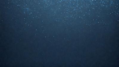 The primary subject of the image is a blue background with a few white specks. The setting appears to be a dark, possibly underwater environment. The visual style is a close-up of the blue background, which gives the image a somewhat surreal and artistic appearance. The colors and mood of the image are predominantly dark and moody, with the blue background and white specks creating a sense of depth and intrigue.