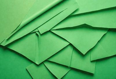 The primary subject of the image is a stack of green paper. The setting is a green background, which creates a vibrant and lively atmosphere. The visual style is a close-up of the paper, showcasing its texture and color. The colors and mood of the image are predominantly green, giving it a fresh and natural feel.