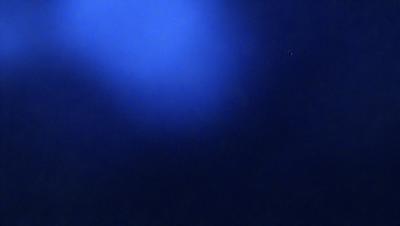 The primary subject of the image is a blue sky with a few clouds. The setting is a dark blue background, which creates a contrasting effect with the lighter blue sky. The visual style is a natural, outdoor scene. The colors and mood of the image are predominantly dark and moody, with the blue sky and clouds providing a sense of depth and tranquility.