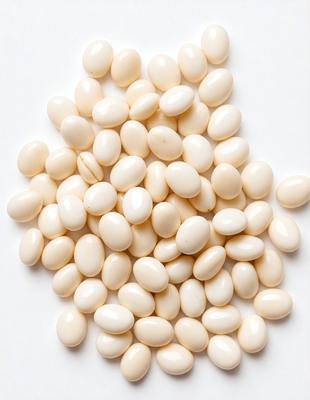 The primary subject of the image is a pile of white, round, and smooth beans. The beans are arranged in a visually appealing manner, creating a sense of abundance and freshness. The setting is a white surface, which provides a clean and uncluttered backdrop for the beans. The visual style of the image is a close-up of the beans, allowing the viewer to appreciate their texture and details. The colors and mood of the image are predominantly white, which gives it
