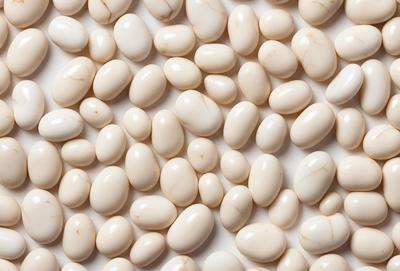 The primary subject of the image is a large number of white, round, and smooth beans. They are arranged in a pattern, covering the entire image. The setting is a white background, which provides a clean and uncluttered appearance. The visual style is a close-up of the beans, showcasing their details and texture. The colors and mood of the image are predominantly white, giving it a clean and fresh appearance.