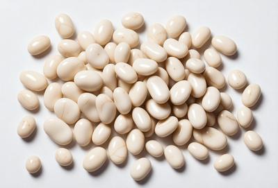 The primary subject of the image is a pile of white beans. The beans are arranged on a white surface, which could be a table or a counter. The setting appears to be a kitchen or a dining area. The visual style of the image is a close-up of the beans, showcasing their texture and details. The colors in the image are predominantly white, giving the scene a clean and simple appearance.