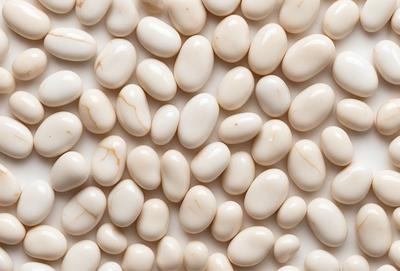 The primary subject of the image is a large number of white beans arranged in a pattern. The beans are placed on a white surface, which could be a wall or a table. The visual style of the image is a close-up of the beans, showcasing their details and texture. The colors and mood of the image are predominantly white, giving it a clean and simple appearance.