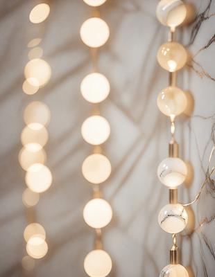 The primary subject of the image is a string of lights, which are illuminated and hanging from a wall. The lights are arranged in a row, creating a visually appealing display. The setting is a white wall, which serves as a clean and neutral backdrop for the lights. The visual style of the image is a close-up of the string of lights, emphasizing their glow and texture. The colors and mood of the image are predominantly white, giving it a clean and minimalist appearance.