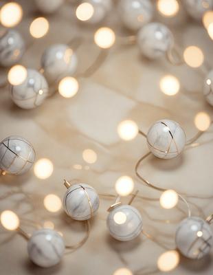 The primary subject of the image is a collection of white and gold ornaments, which are likely Christmas lights. These ornaments are arranged in a pattern, creating a visually appealing display. The setting is a white surface, which provides a clean and elegant backdrop for the ornaments. The visual style of the image is a close-up of the ornaments, showcasing their intricate details and textures. The colors and mood of the image are predominantly white and gold, giving it a warm and festive atmosphere