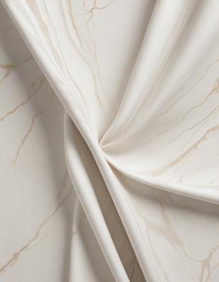 The primary subject of the image is a white sheet of fabric, possibly a curtain or a tablecloth. The setting is a room with a marble wall, which adds a luxurious and elegant touch to the scene. The visual style is a close-up of the fabric, showcasing its texture and details. The colors and mood of the image are predominantly white, giving it a clean and sophisticated appearance.