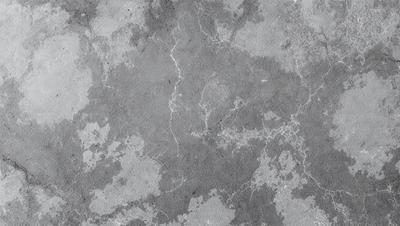 The primary subject of the image is a large, textured surface with a patterned texture. The setting is a concrete wall, and the visual style is a close-up of the wall. The colors and mood of the image are predominantly gray, giving it a somewhat dull and industrial appearance.