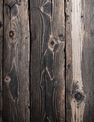 The primary subject of the image is a wooden floor with a unique pattern of holes. The setting is a room with a wooden floor, and the visual style is a close-up of the wooden surface. The dominant colors are brown and black, giving the floor a rustic and natural appearance. The overall atmosphere of the image is one of warmth and texture, as the wooden floor stands out as the main focus of the scene.