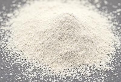 The primary subject of the image is a pile of white powder, which appears to be flour. The setting is a table, and the visual style is a close-up of the flour. The colors in the image are predominantly white, giving the scene a clean and simple appearance.