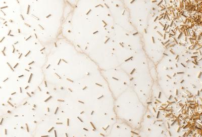 The primary subject of the image is a marble table with a pattern of gold nails or gold studs on it. The setting is a white marble surface, which provides a clean and elegant backdrop for the gold nails. The visual style is a close-up of the marble table, showcasing the intricate pattern of the gold nails. The colors and mood of the image are predominantly gold and white, creating a warm and sophisticated atmosphere.