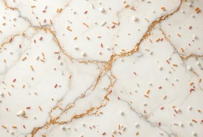 The primary subject of the image is a marble countertop with a variety of candy and donut decorations on it. The setting is a kitchen or dining area, with the marble countertop serving as the main focus. The visual style is a combination of photo and digital art, creating a unique and eye-catching design. The colors and mood of the image are predominantly white and gold, giving it a luxurious and inviting atmosphere.