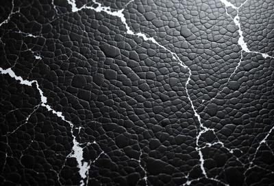 The primary subject of the image is a close-up of a black leather surface with a pattern of white spots. The setting is a black background, and the visual style appears to be a photo. The dominant colors are black and white, creating a moody atmosphere.
