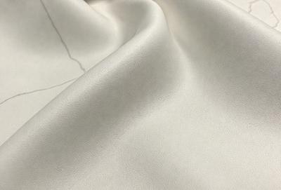 The primary subject of the image is a piece of leather, which is the main object, scene, or focus of the image. The leather is displayed in a close-up view, showcasing its texture and details. The setting or background of the image is a white surface, which provides a clean and minimalist backdrop for the leather. The visual style of the image is a close-up, which emphasizes the texture and details of the leather. The colors and mood of the image are predominantly neutral