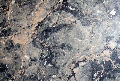 The primary subject of the image is a marble surface with a pattern of holes and bumps. The setting is a stone wall, and the visual style is a close-up of the marble surface. The colors and mood of the image are predominantly dark, with the marble surface being the main focus.