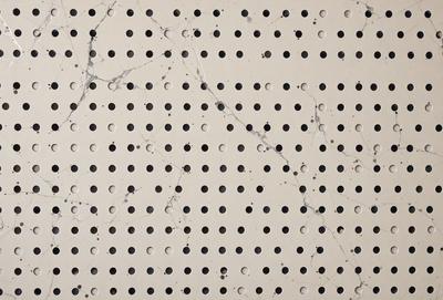 The primary subject of the image is a wall with a pattern of holes. The setting is a room with a white surface, and the visual style appears to be a combination of a photo and a drawing. The dominant colors are white and grey, creating a clean and minimalist atmosphere.