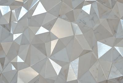 The primary subject of the image is a white marble wall with a geometric pattern. The setting is a room with a white marble surface, which adds to the overall visual style. The image is a photo, capturing the intricate details of the marble wall. The colors and mood of the image are predominantly white, giving it a clean and elegant appearance.