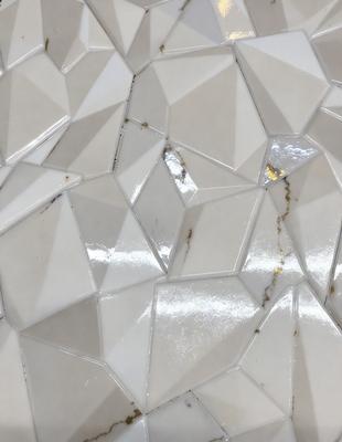 The primary subject of the image is a white tile with a pattern of triangles. The setting is a wall, and the visual style appears to be a photo. The dominant colors are white and grey, creating a clean and minimalist atmosphere.