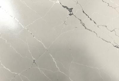 The primary subject of the image is a marble countertop with a large crack in it. The setting is a room with a grey background. The visual style is a close-up of the marble countertop, showcasing the crack and the marble's texture. The colors and mood of the image are predominantly grey, with the crack in the marble adding a sense of imperfection to the otherwise elegant surface.
