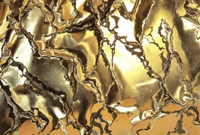 The primary subject of the image is a gold-colored metal surface, which appears to be a piece of art or a decorative item. The setting is a room with a wall that features the gold-colored metal surface. The visual style of the image is a close-up of the gold-colored metal, showcasing its intricate design and texture. The colors and mood of the image are predominantly gold and warm, creating a sense of luxury and sophistication.