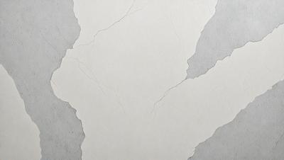 The primary subject of the image is a white wall with a pattern of cracks and holes. The setting is a room with a grey background. The visual style is a close-up of the wall, showcasing the cracks and holes. The colors and mood of the image are predominantly neutral, with the white wall and grey background creating a calm and minimalist atmosphere.