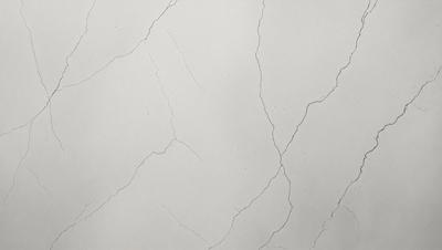 The primary subject of the image is a white marble wall with visible cracks and crevices. The setting is a room with a white background, which adds to the stark contrast between the wall and the rest of the space. The visual style is a close-up of the wall, showcasing the intricate details of the marble. The colors and mood of the image are predominantly white, giving it a clean and minimalist appearance.