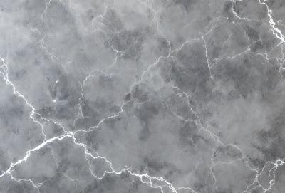 The primary subject of the image is a marble surface with a pattern of lightning bolts. The setting is a gray and white marble wall, which serves as the background. The visual style is a close-up of the marble surface, showcasing the lightning bolts pattern. The colors and mood of the image are predominantly gray and white, with the lightning bolts adding a touch of contrast and interest.