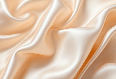 The primary subject of the image is a close-up of a piece of silk fabric. The setting is a room with a pink background, which adds a warm and inviting atmosphere to the scene. The visual style is a realistic representation of the silk fabric, showcasing its texture and details. The colors and mood of the image are predominantly pink, creating a sense of luxury and elegance.
