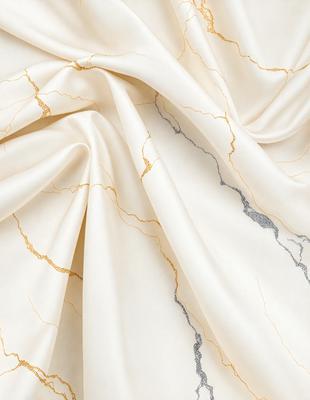 The primary subject of the image is a white fabric with gold accents. The setting is a marble surface, which adds a luxurious and elegant touch to the scene. The visual style is a close-up of the fabric, showcasing its intricate details and textures. The colors and mood of the image are predominantly white and gold, creating a sense of sophistication and refinement.