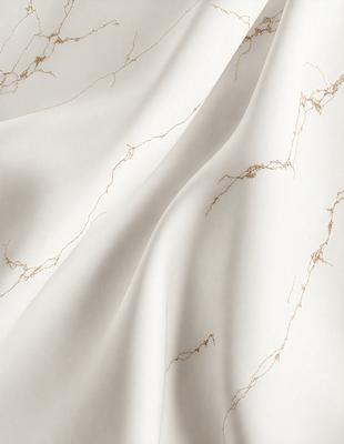 The primary subject of the image is a white sheet of fabric, possibly a tablecloth or a curtain. The setting is a room with a marble wall, which adds a luxurious and elegant touch to the scene. The visual style is a close-up of the fabric, showcasing its texture and details. The colors in the image are predominantly white, which creates a clean and minimalist atmosphere.
