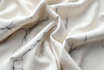 The primary subject of the image is a white sheet of fabric with a marble pattern. The setting is a white background, and the visual style is a close-up of the fabric. The colors and mood of the image are predominantly white, giving it a clean and elegant appearance.