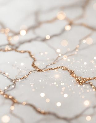 The primary subject of the image is a close-up of a gold glittery substance, possibly a gold glitter paper or a gold glitter paint, on a white surface. The setting appears to be a white table or countertop. The visual style of the image is a close-up of the glittery substance, which gives it a unique and eye-catching appearance. The colors and mood of the image are predominantly white and gold, creating a warm and inviting atmosphere.